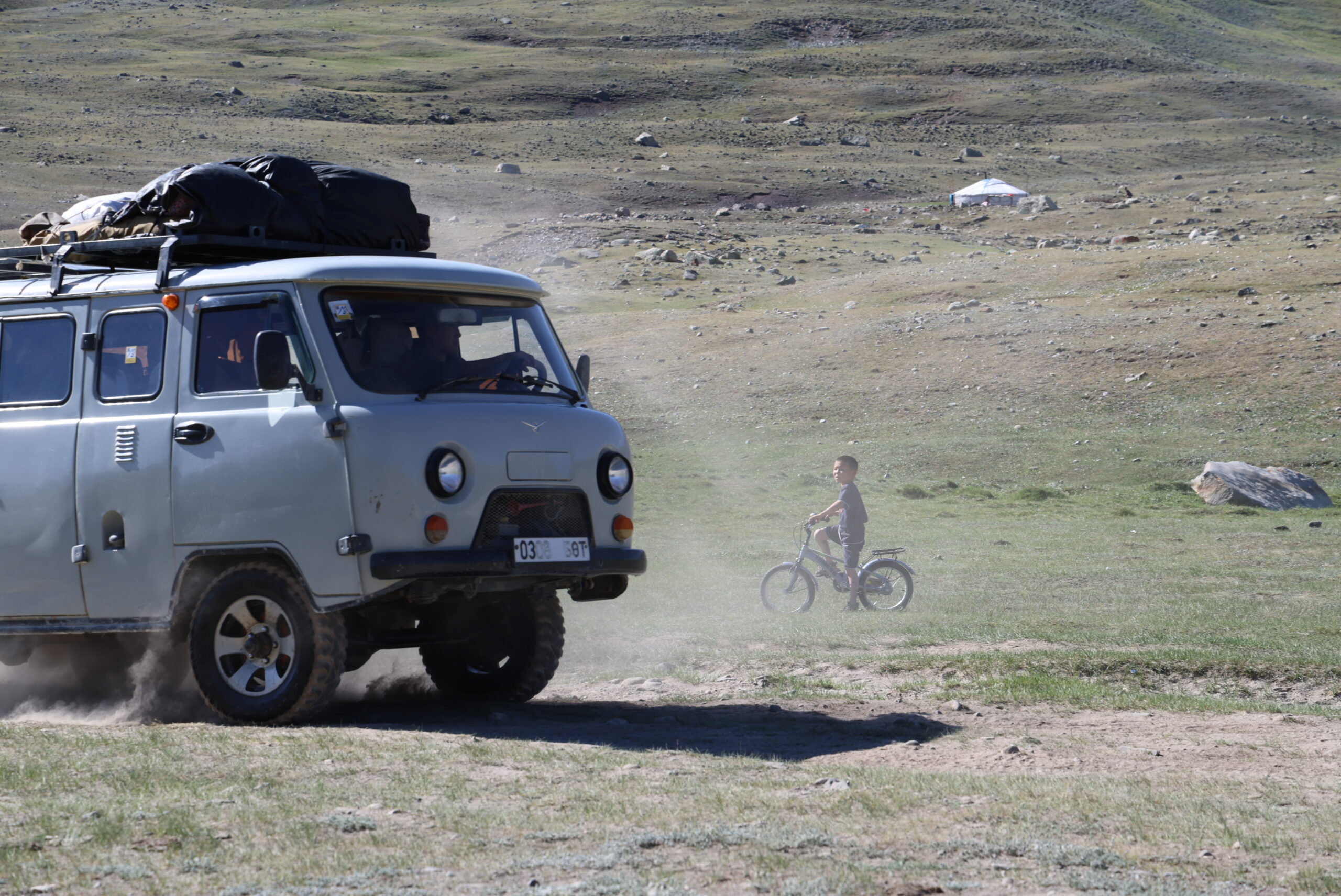 Gray UAZ van with a white Mongolian license plate driving across the steppe.